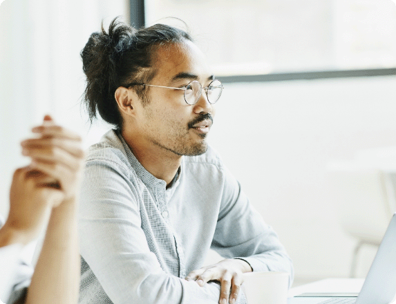 Professional seated at a table in a bright meeting room, listening attentively during a discussion with a laptop open nearby